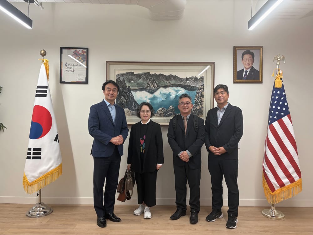 Four people standing between the Korean and U.S. flags at the Consulate General of the Republic of Korea in New York.