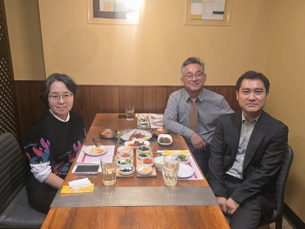 Three people seated at a restaurant table set with Korean side dishes.